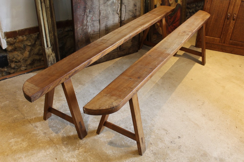 A pair of long 19th-century French fruitwood refectory benches featuring A-frame trestle legs and pegged joinery. View IX
