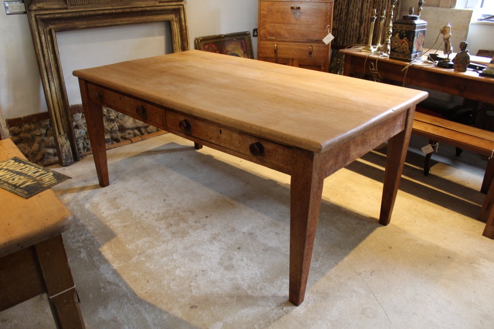 A late Victorian oak farmhouse dining table featuring a plain rectangular top, frieze drawers with wooden turned knobs, and square tapered legs.