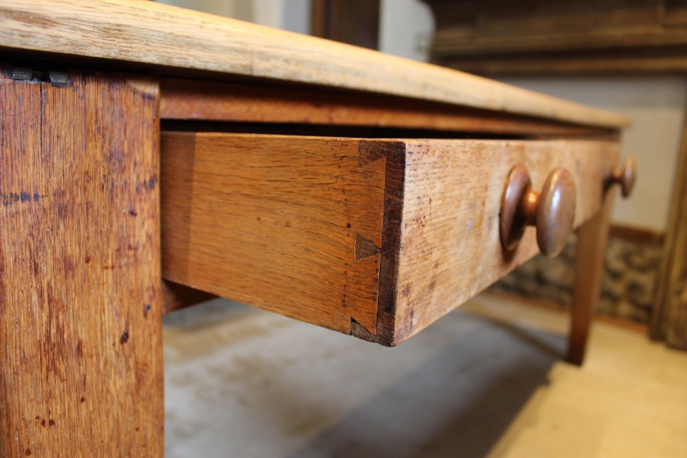 A late Victorian oak farmhouse dining table featuring a plain rectangular top, frieze drawers with wooden turned knobs, and square tapered legs. View V