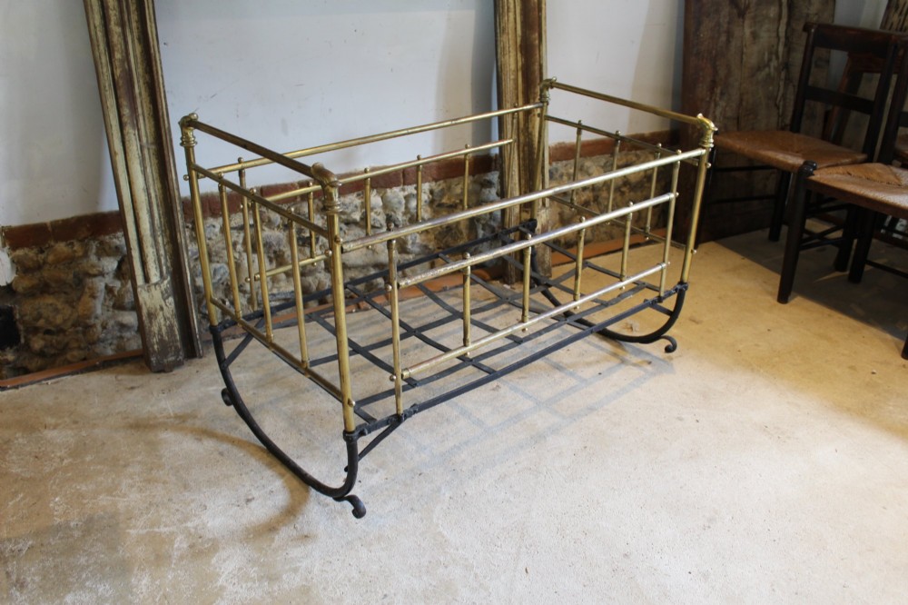 A Victorian brass and black wrought iron rocking cot featuring tubular side rails, finial accents, and a curved iron base.