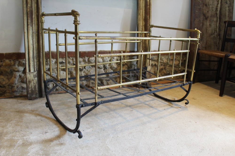 A Victorian brass and black wrought iron rocking cot featuring tubular side rails, finial accents, and a curved iron base. View V