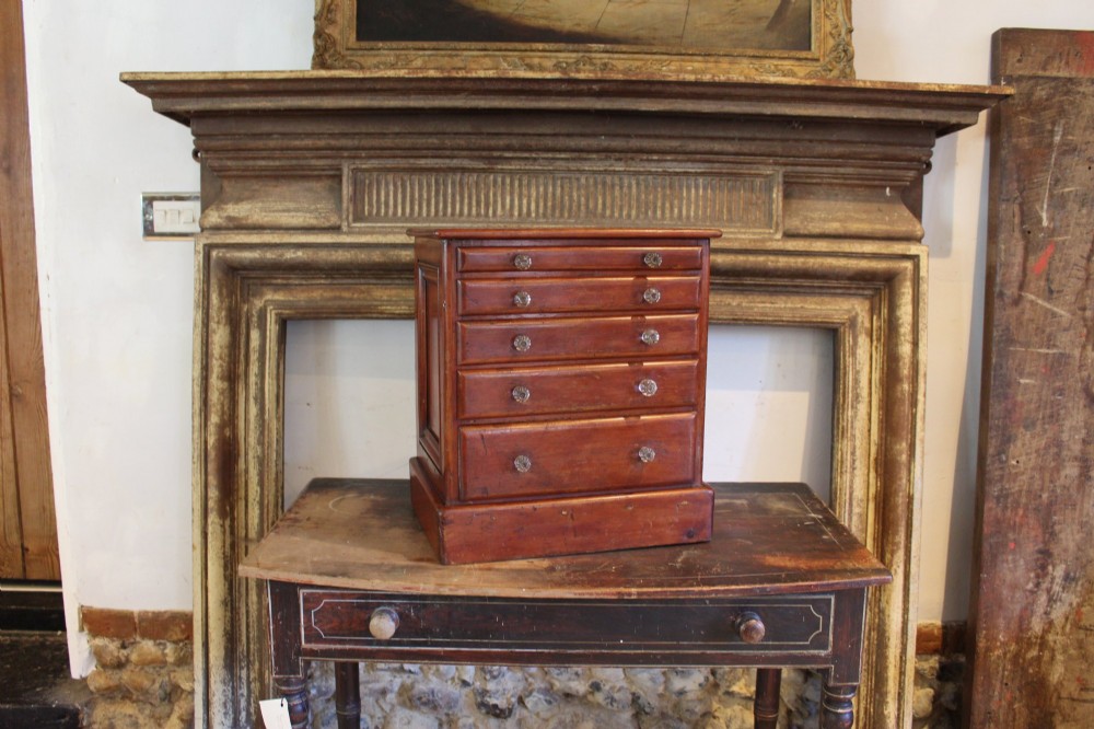 A Victorian miniature wooden chest of five graduated drawers with small metal knobs and a solid base.