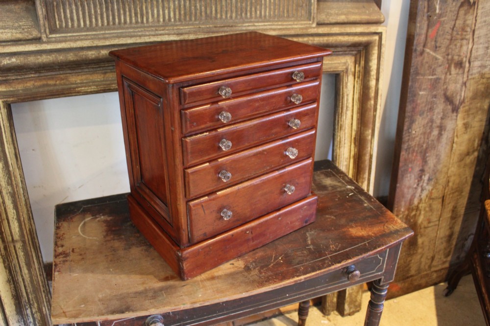 A Victorian miniature wooden chest of five graduated drawers with small metal knobs and a solid base. View II