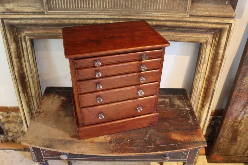 A Victorian miniature wooden chest of five graduated drawers with small metal knobs and a solid base. View III