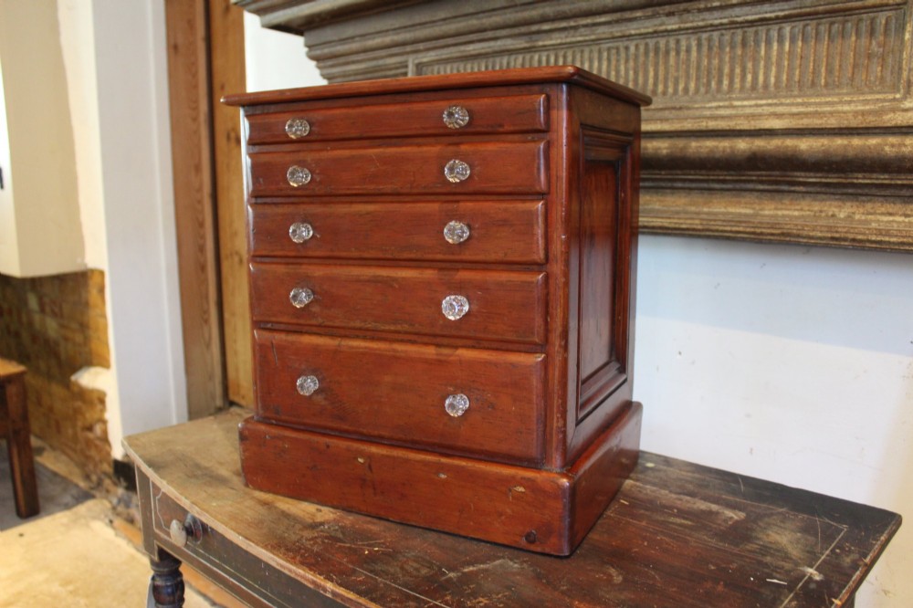 A Victorian miniature wooden chest of five graduated drawers with small metal knobs and a solid base. View IV