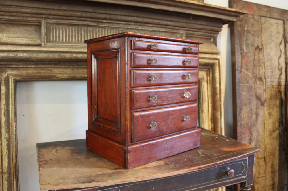 A Victorian miniature wooden chest of five graduated drawers with small metal knobs and a solid base. View VIII