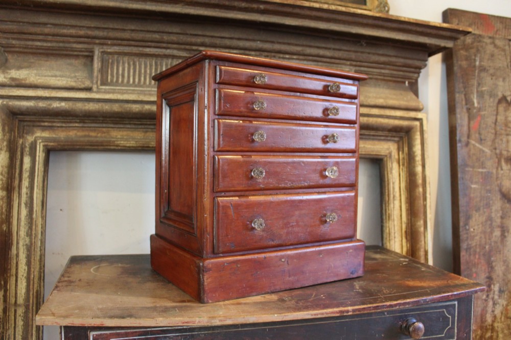 A Victorian miniature wooden chest of five graduated drawers with small metal knobs and a solid base. View IX