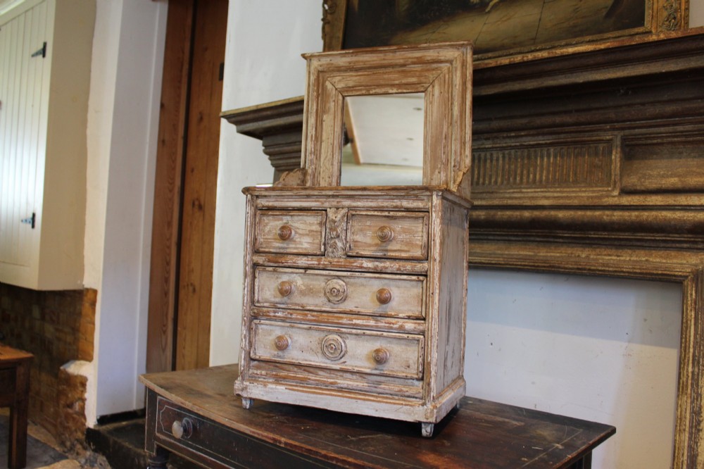 A late 19th-century French miniature wooden chest of drawers featuring a painted distressed cream finish, small turned wooden knobs, and an attached swivel mirror. View II