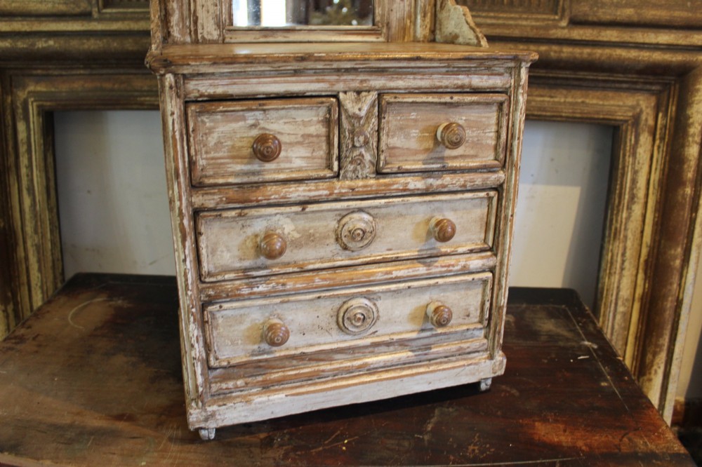A late 19th-century French miniature wooden chest of drawers featuring a painted distressed cream finish, small turned wooden knobs, and an attached swivel mirror. View V