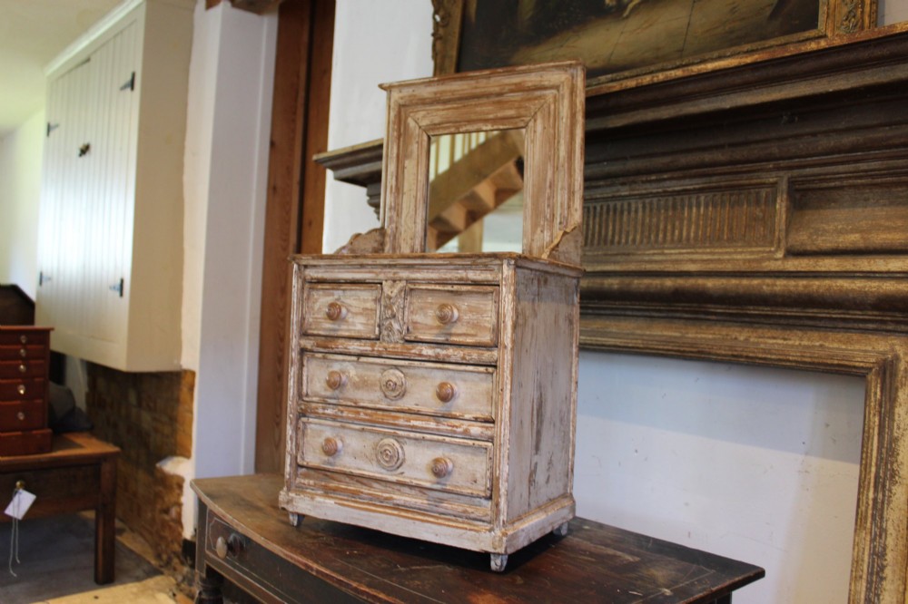 A late 19th-century French miniature wooden chest of drawers featuring a painted distressed cream finish, small turned wooden knobs, and an attached swivel mirror. View VIII
