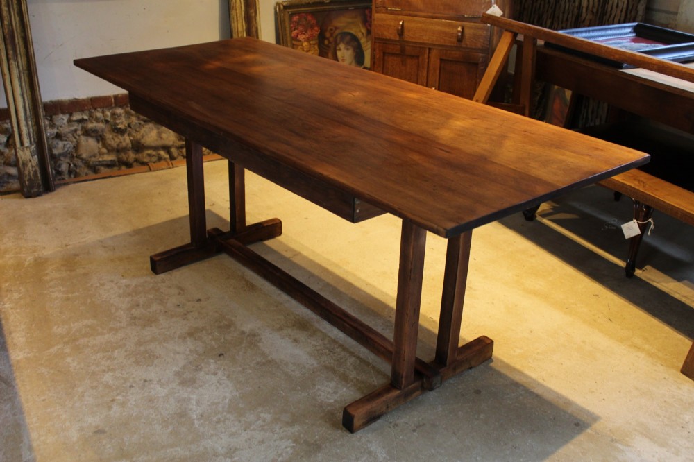 A solid teak Arts and Crafts refectory table featuring twin upright trestle supports resting on shoe feet and joined by a low stretcher rail. View II