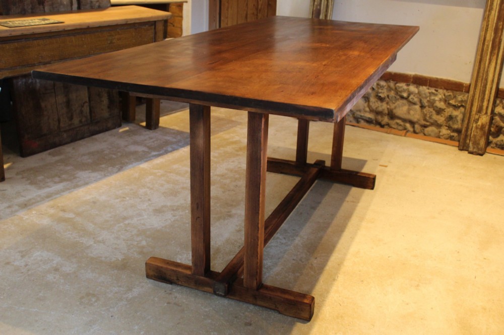 A solid teak Arts and Crafts refectory table featuring twin upright trestle supports resting on shoe feet and joined by a low stretcher rail. View IV