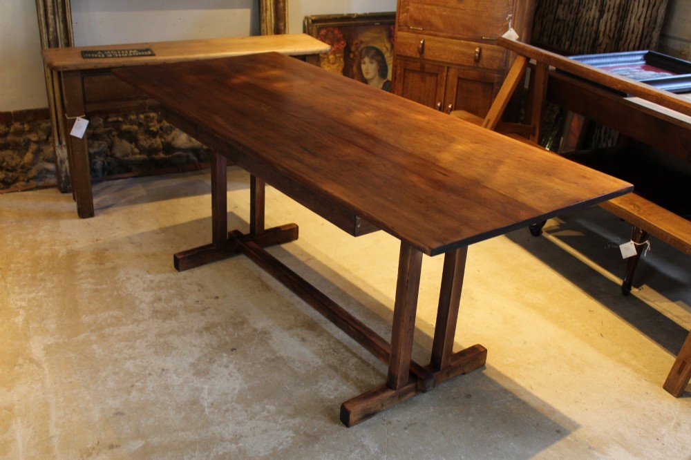 A solid teak Arts and Crafts refectory table featuring twin upright trestle supports resting on shoe feet and joined by a low stretcher rail. View VI