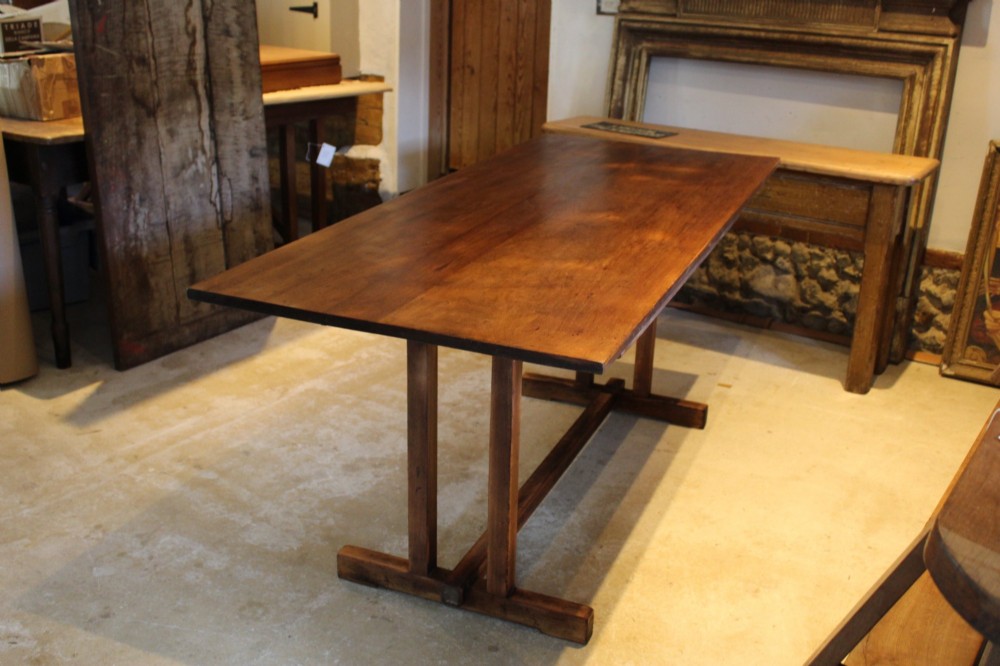 A solid teak Arts and Crafts refectory table featuring twin upright trestle supports resting on shoe feet and joined by a low stretcher rail. View VII