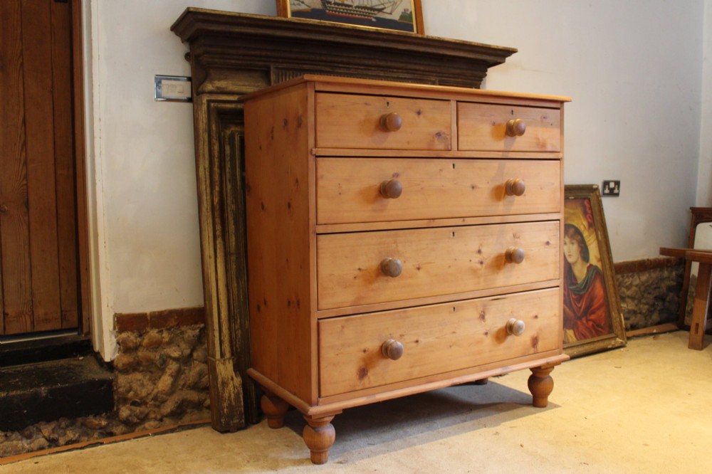 A Victorian pine chest of drawers featuring two short drawers over three long drawers with turned wooden handles and turned bun feet.