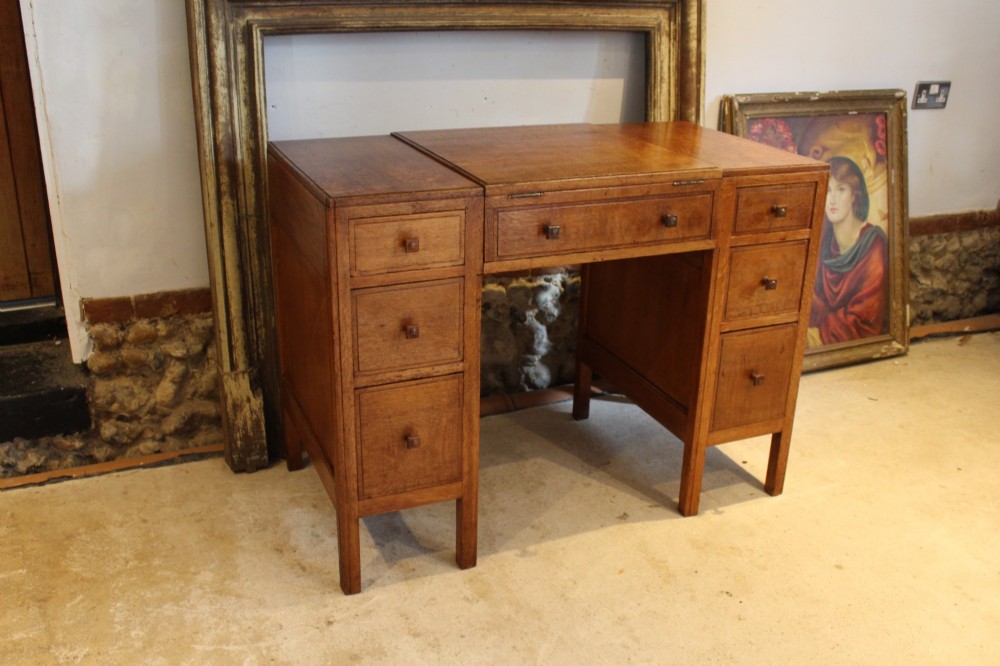 An antique golden oak dressing table featuring a central flip-top section, side drawer pedestals, and square wooden handles.