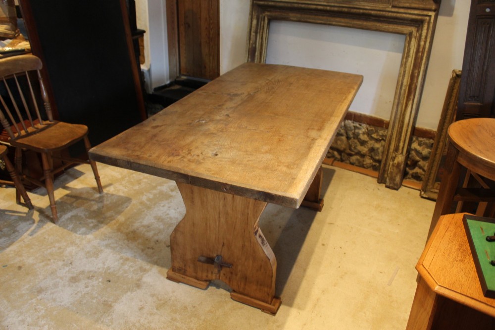 A solid oak refectory dining table featuring a rectangular plank top and a trestle base with a central stretcher held by a wedge.