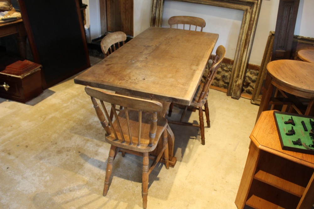 A solid oak refectory dining table featuring a rectangular plank top and a trestle base with a central stretcher held by a wedge. View II