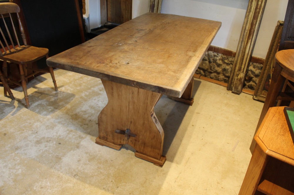 A solid oak refectory dining table featuring a rectangular plank top and a trestle base with a central stretcher held by a wedge. View III