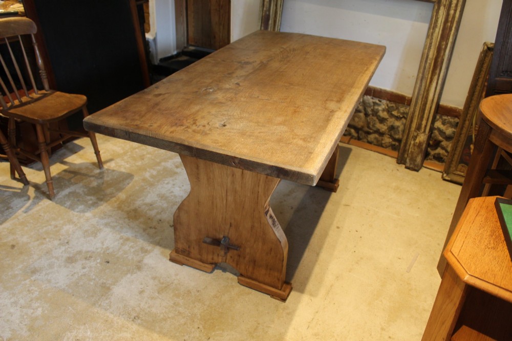 A solid oak refectory dining table featuring a rectangular plank top and a trestle base with a central stretcher held by a wedge. View VII