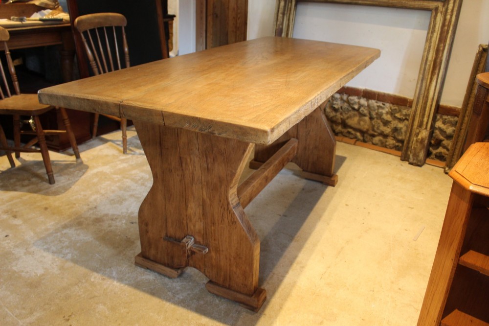 An antique solid oak refectory dining table featuring a thick rectangular top supported by shaped trestle end supports connected by a low stretcher with keyed tenons.