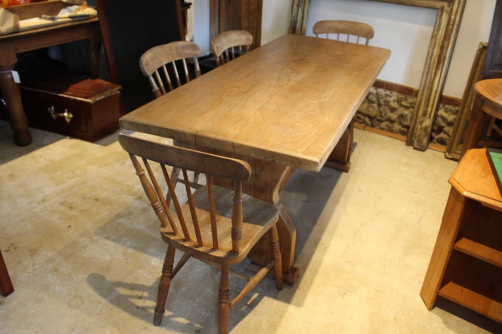 An antique solid oak refectory dining table featuring a thick rectangular top supported by shaped trestle end supports connected by a low stretcher with keyed tenons. View III