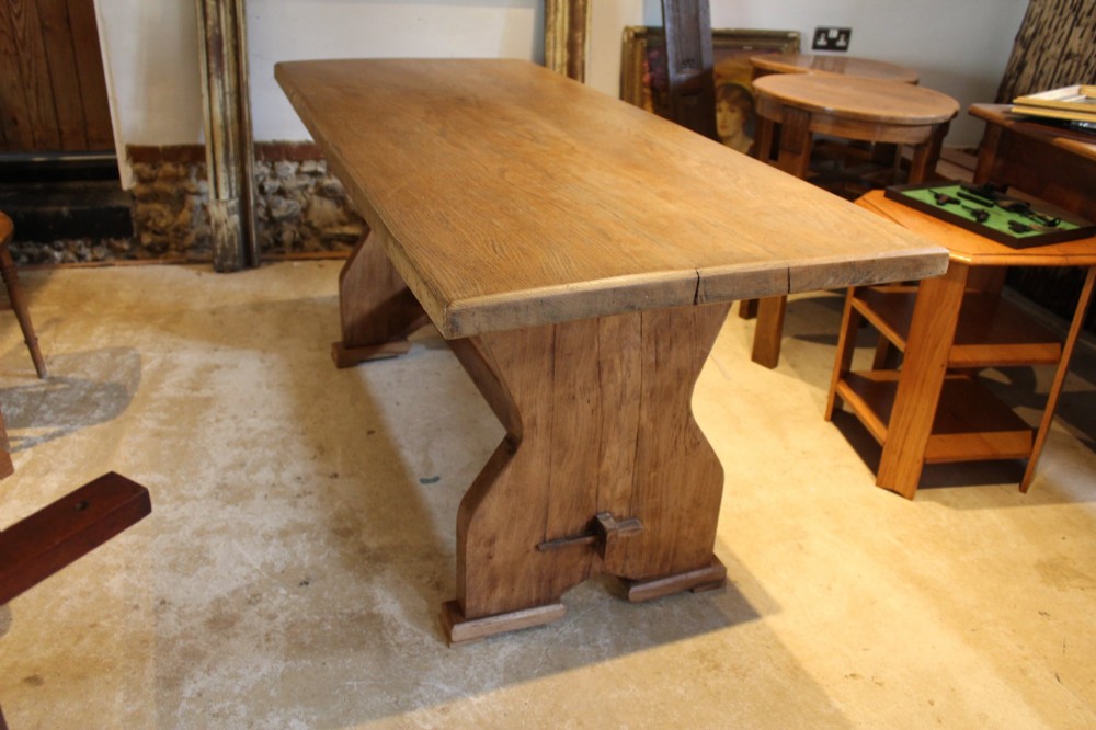An antique solid oak refectory dining table featuring a thick rectangular top supported by shaped trestle end supports connected by a low stretcher with keyed tenons. View IV