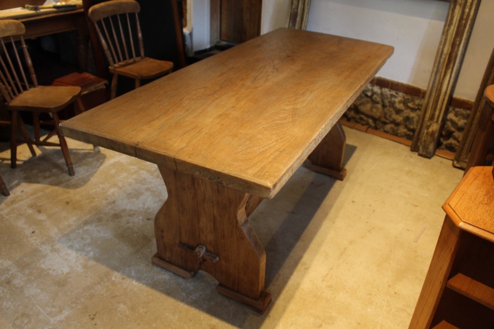 An antique solid oak refectory dining table featuring a thick rectangular top supported by shaped trestle end supports connected by a low stretcher with keyed tenons. View VII