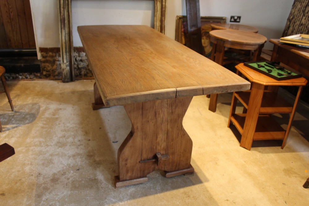 An antique solid oak refectory dining table featuring a thick rectangular top supported by shaped trestle end supports connected by a low stretcher with keyed tenons. View IX