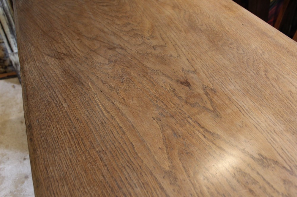 An antique solid oak refectory dining table featuring a thick rectangular top supported by shaped trestle end supports connected by a low stretcher with keyed tenons. View X