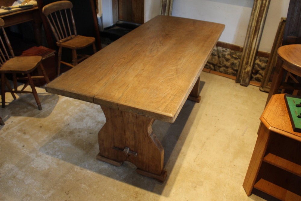 An antique solid oak refectory dining table featuring a thick rectangular top supported by shaped trestle end supports connected by a low stretcher with keyed tenons. View XI