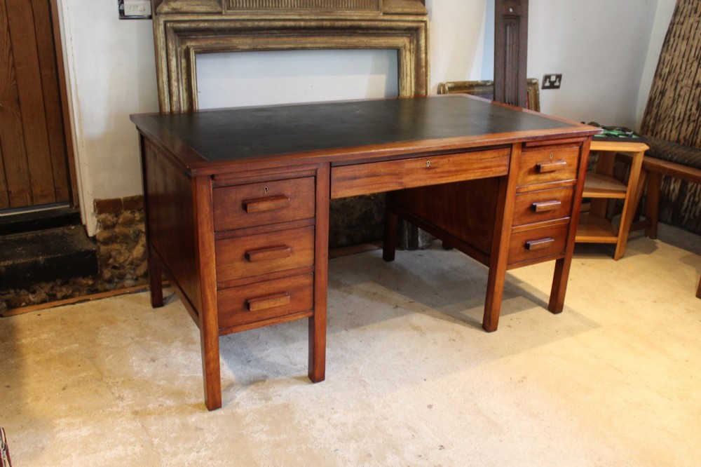 An Art Deco walnut pedestal desk featuring a black leather inset top, a central drawer, and six side drawers with wooden bar handles.