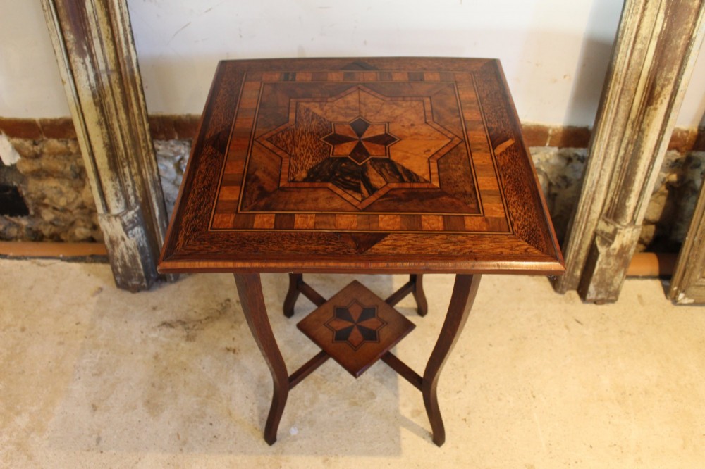 A square Victorian side table featuring geometric star-patterned specimen wood marquetry, curved legs, and a matching central undertier.