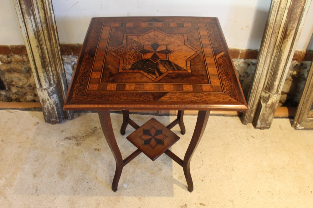 A square Victorian side table featuring geometric star-patterned specimen wood marquetry, curved legs, and a matching central undertier. View VI