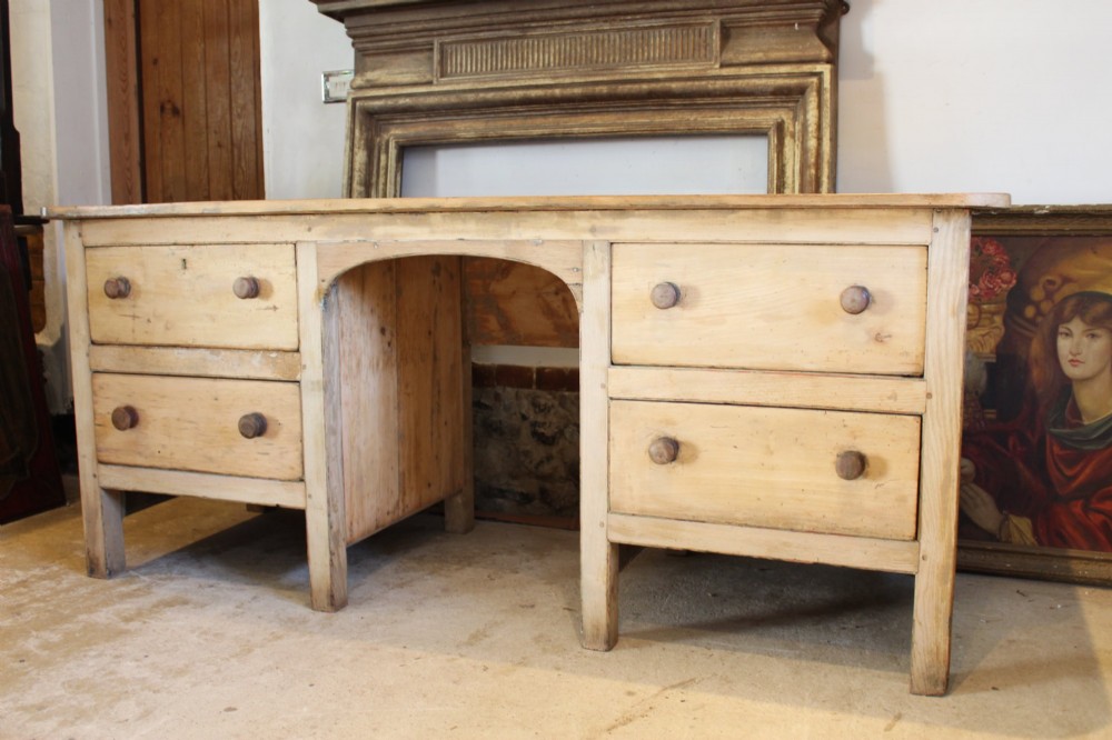 A George III scrubbed pine kneehole desk featuring four side drawers with turned wood handles and an arched central opening.