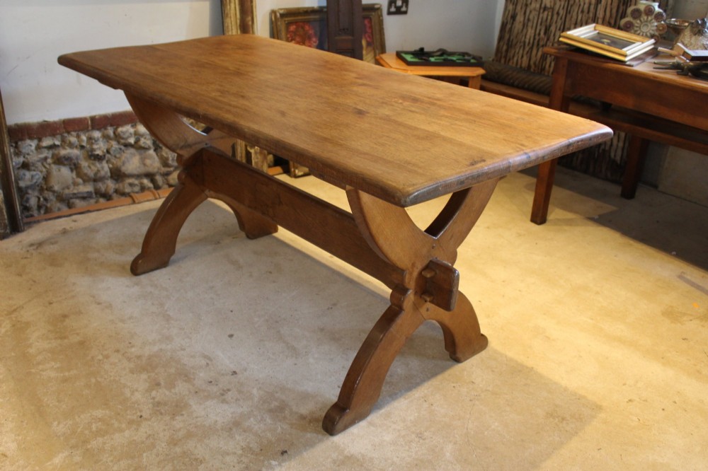 An Arts and Crafts solid oak refectory dining table featuring curved trestle legs and a pegged stretcher.