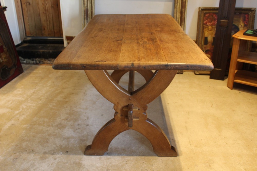 An Arts and Crafts solid oak refectory dining table featuring curved trestle legs and a pegged stretcher. View II