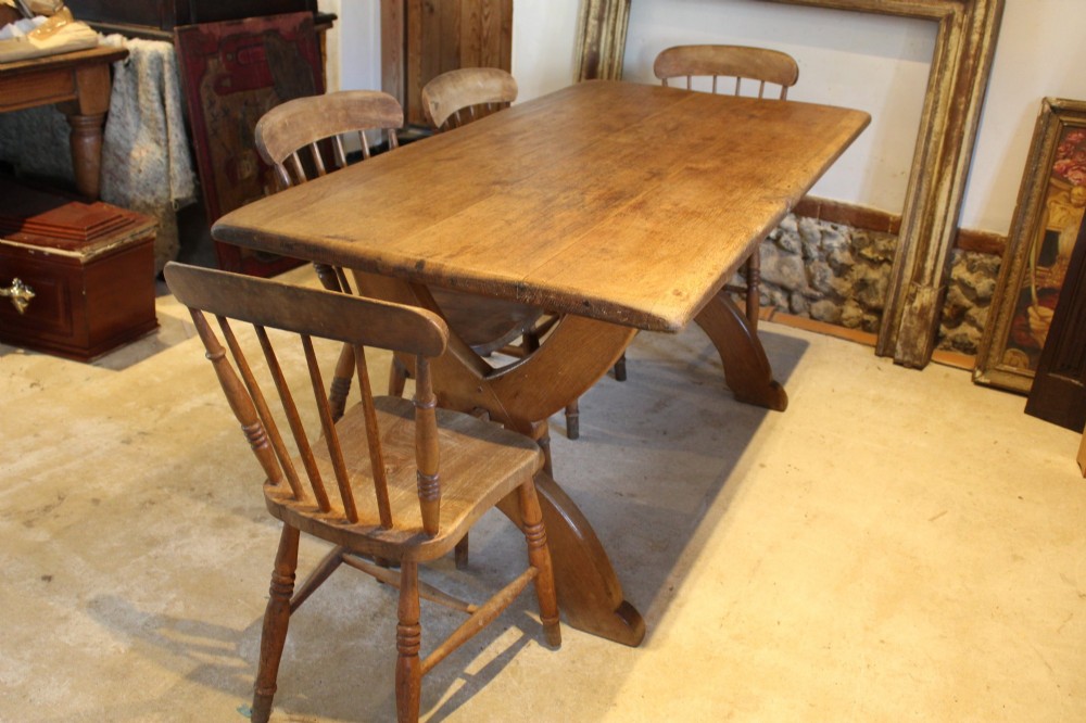 An Arts and Crafts solid oak refectory dining table featuring curved trestle legs and a pegged stretcher. View III