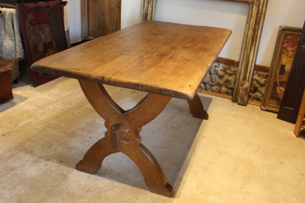 An Arts and Crafts solid oak refectory dining table featuring curved trestle legs and a pegged stretcher. View V