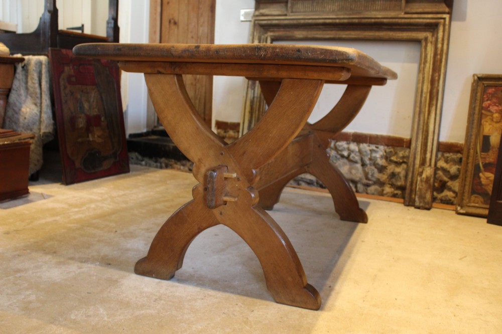 An Arts and Crafts solid oak refectory dining table featuring curved trestle legs and a pegged stretcher. View VI
