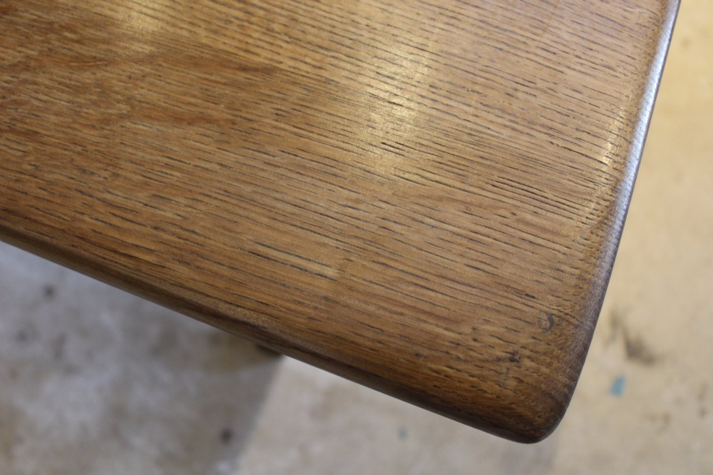 An Arts and Crafts solid oak refectory dining table featuring curved trestle legs and a pegged stretcher. View IX