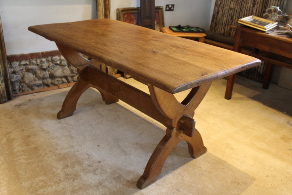An Arts and Crafts solid oak refectory dining table featuring curved trestle legs and a pegged stretcher. View X