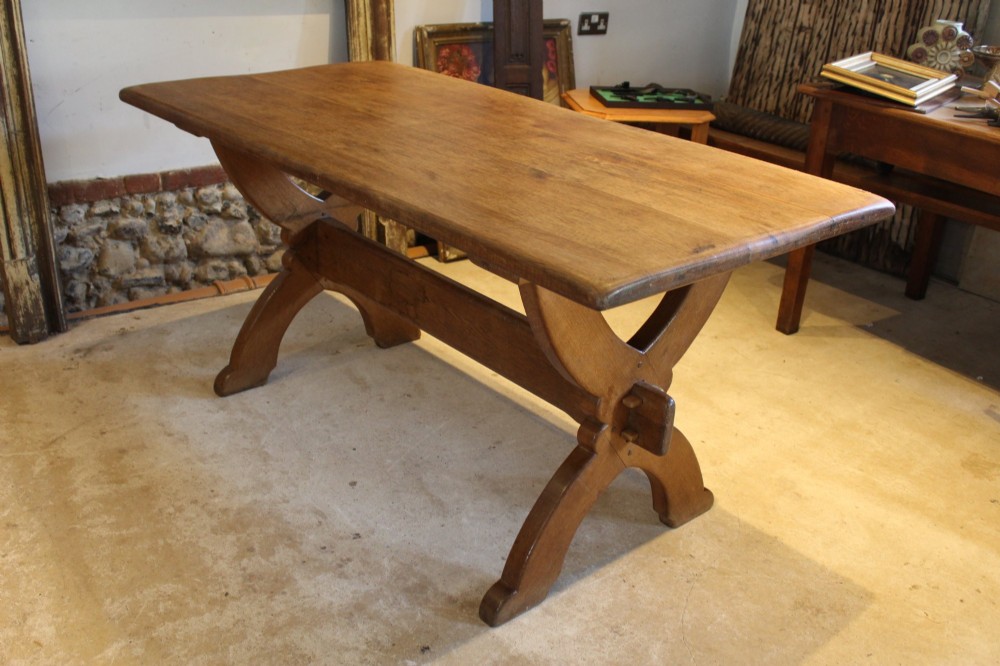 An Arts and Crafts solid oak refectory dining table featuring curved trestle legs and a pegged stretcher. View XI