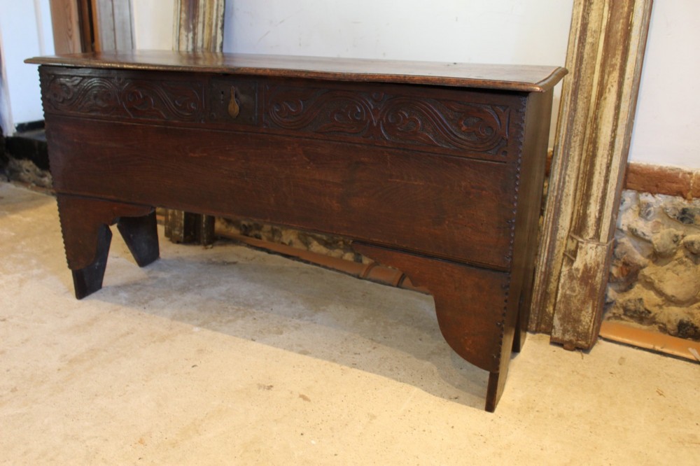 A dark elm six-plank coffer featuring a carved scrollwork frieze along the upper front rail, an iron escutcheon, and cutout boot-jack end supports. View II