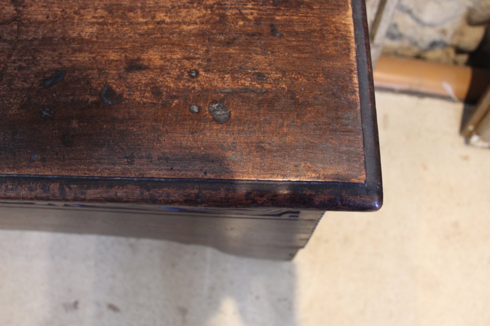 A dark elm six-plank coffer featuring a carved scrollwork frieze along the upper front rail, an iron escutcheon, and cutout boot-jack end supports. View III