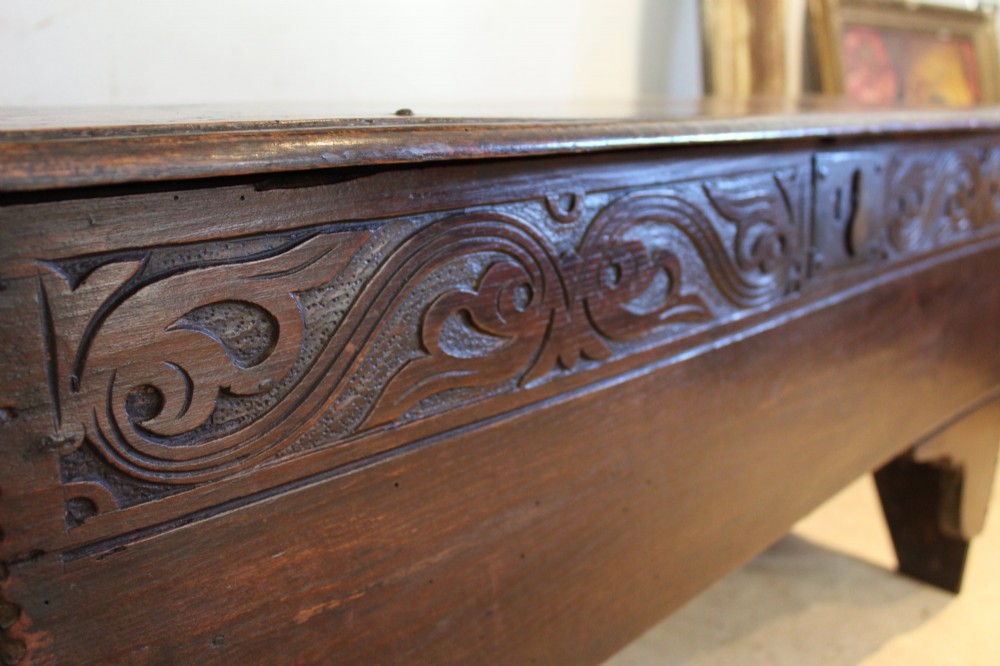 A dark elm six-plank coffer featuring a carved scrollwork frieze along the upper front rail, an iron escutcheon, and cutout boot-jack end supports. View IV