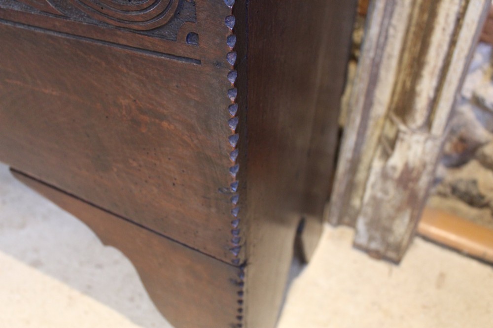 A dark elm six-plank coffer featuring a carved scrollwork frieze along the upper front rail, an iron escutcheon, and cutout boot-jack end supports. View VIII