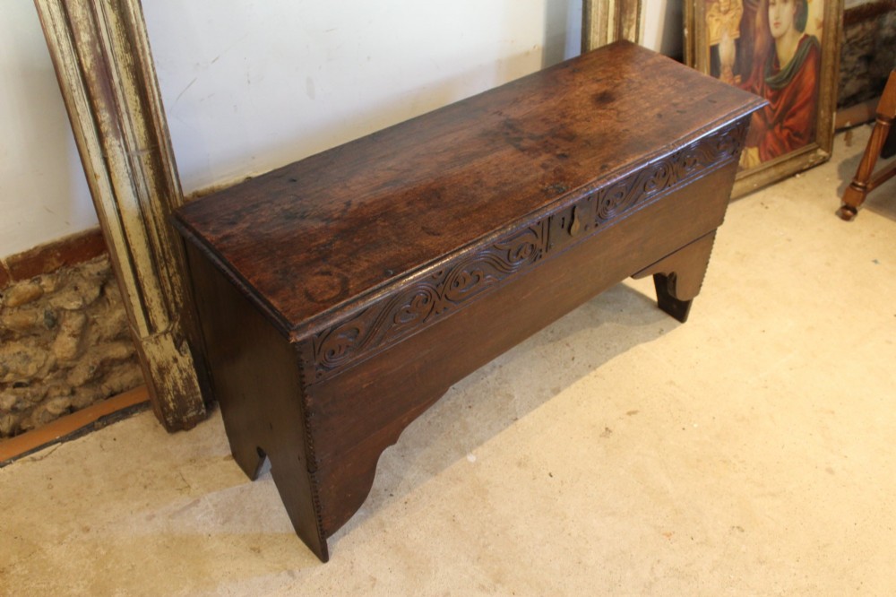 A dark elm six-plank coffer featuring a carved scrollwork frieze along the upper front rail, an iron escutcheon, and cutout boot-jack end supports. View IX