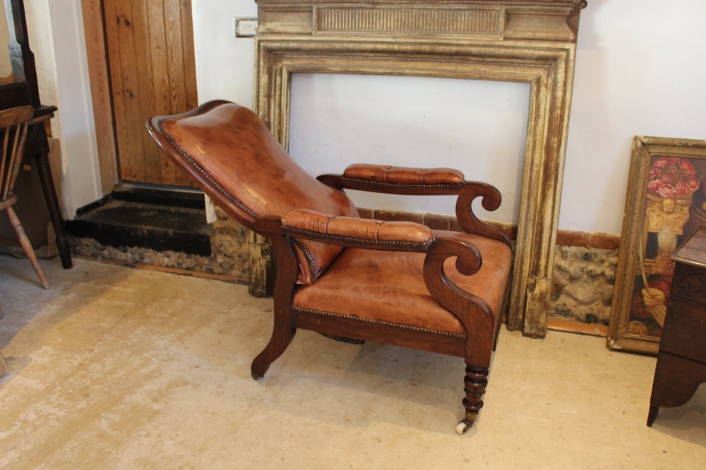 A William IV leather reclining armchair with carved mahogany frame, scrolled arms, brass stud trim, turned front legs, and castors. View II