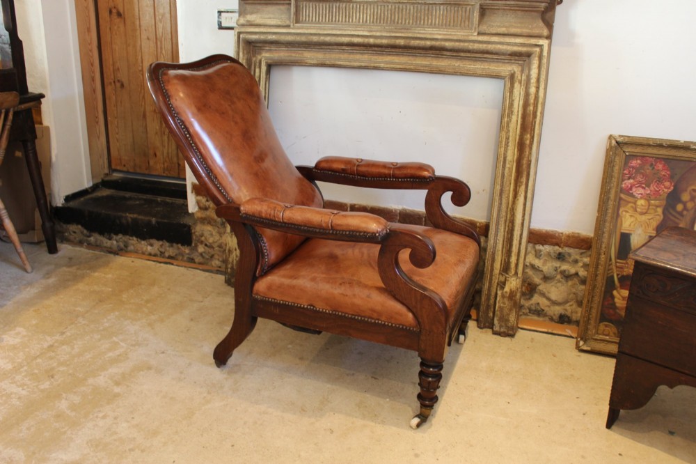 A William IV leather reclining armchair with carved mahogany frame, scrolled arms, brass stud trim, turned front legs, and castors. View III
